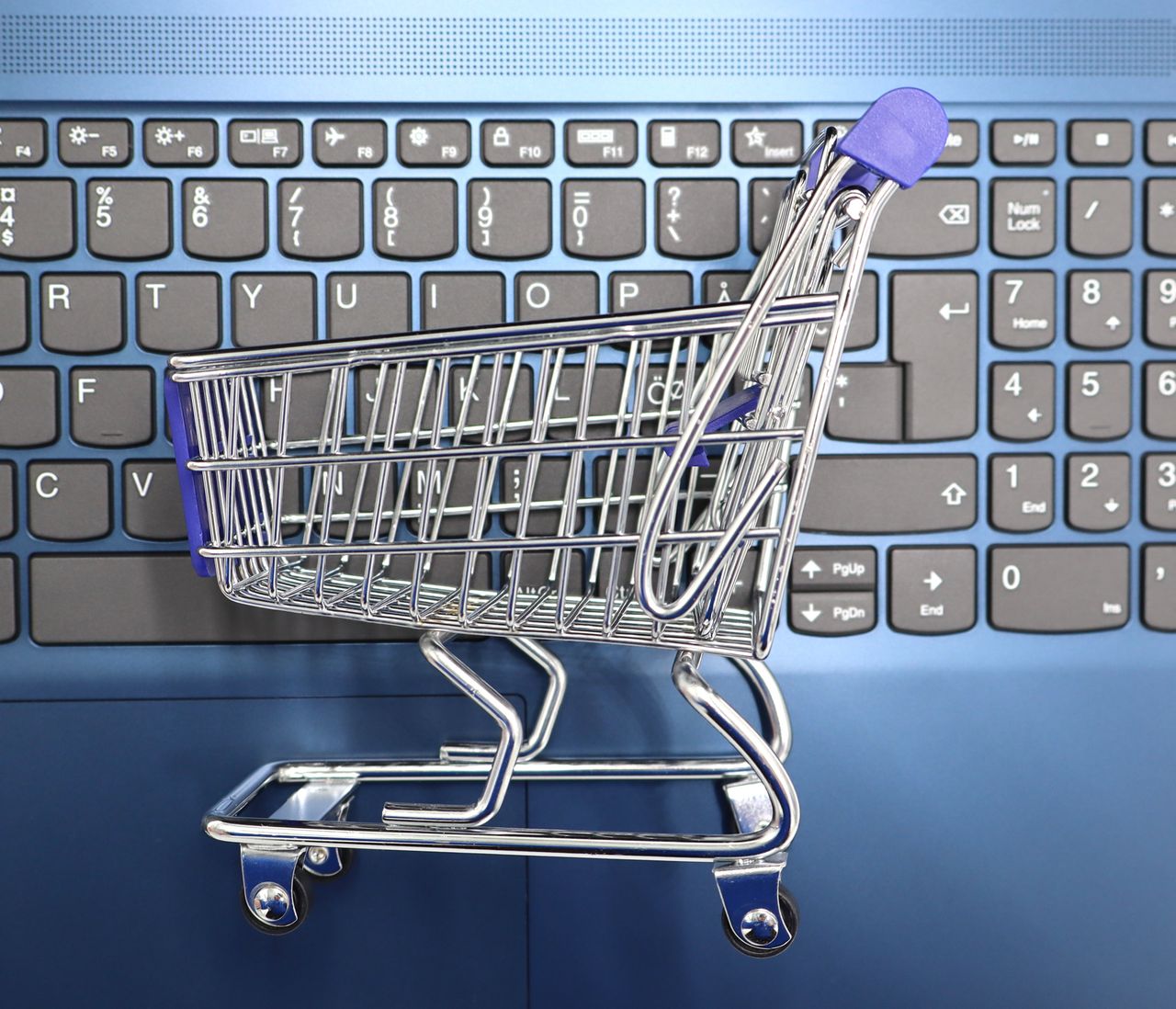 Une mini-caisse de shopping posée sur le clavier d’un ordinateur portable, symbolisant les achats en ligne et le commerce électronique.